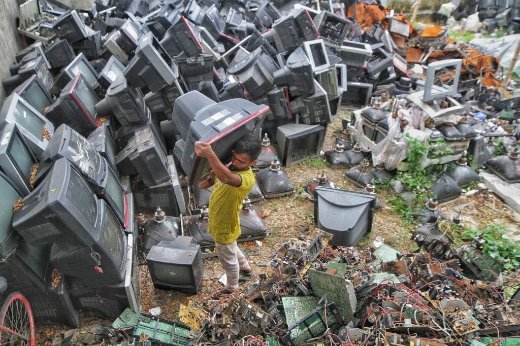 Informal worker carries a used television on his shoulder amidst e-waste dumpage